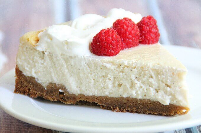 Vegan Vanilla Bean Cheesecake slice with raspberries and coconut whipped cream.