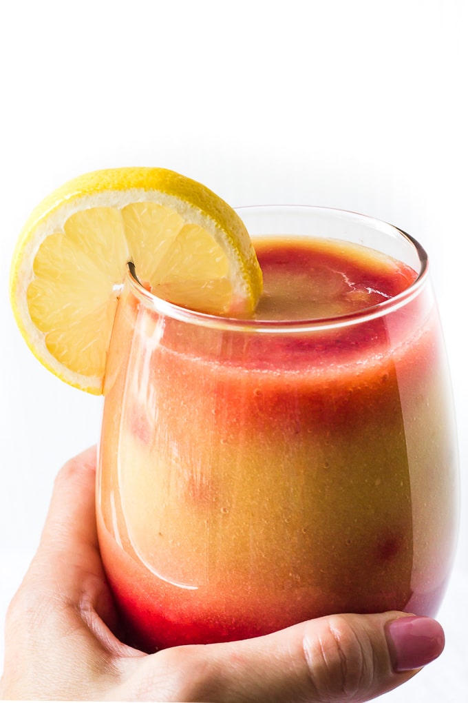 A hand holding a glass of a sunrise detox smoothie.