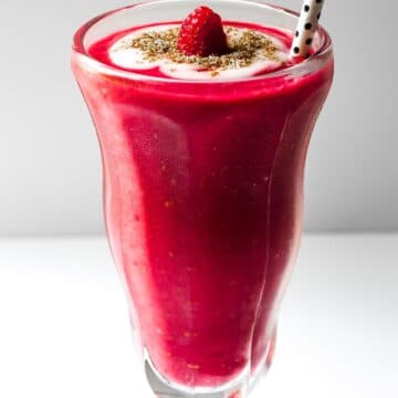 A glass filled with a raspberry smoothie and a drinking straw.