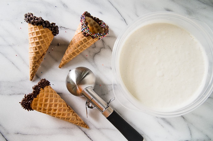 3 waffle cones dipped in chocolate next to vanilla ice cream