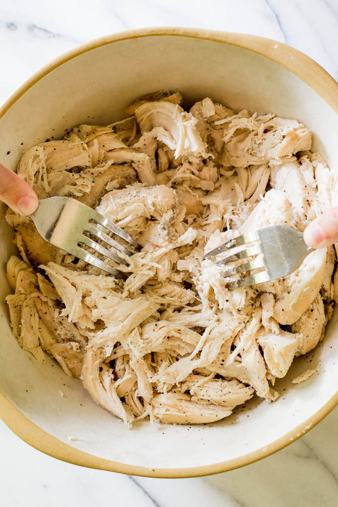 Chicken being shredded in a bowl with fork.