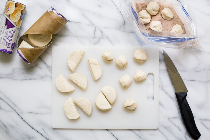 A cutting board with unbaked biscuit dough being cut into quarters.