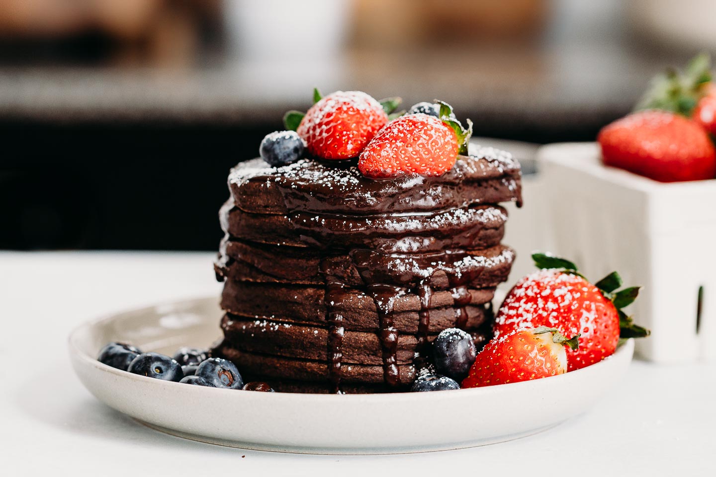 A stack of chocolate pancakes on a plate with syrup.