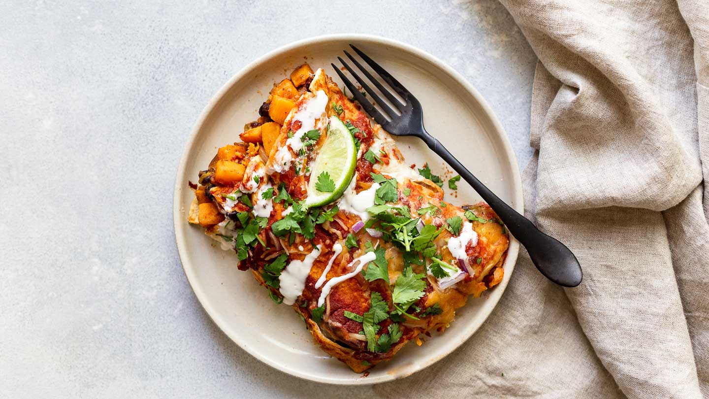 Two sweet potato enchiladas on a plate with a fork and napkin.