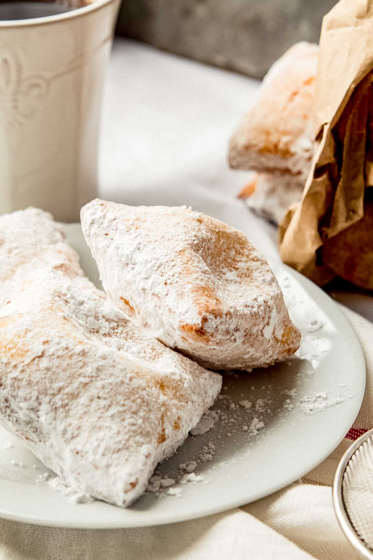 Beignets on a plate with a cup of coffee on the side.