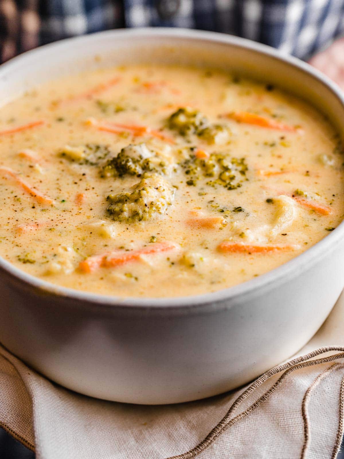 A woman holding a bowl of broccoli cheese soup.