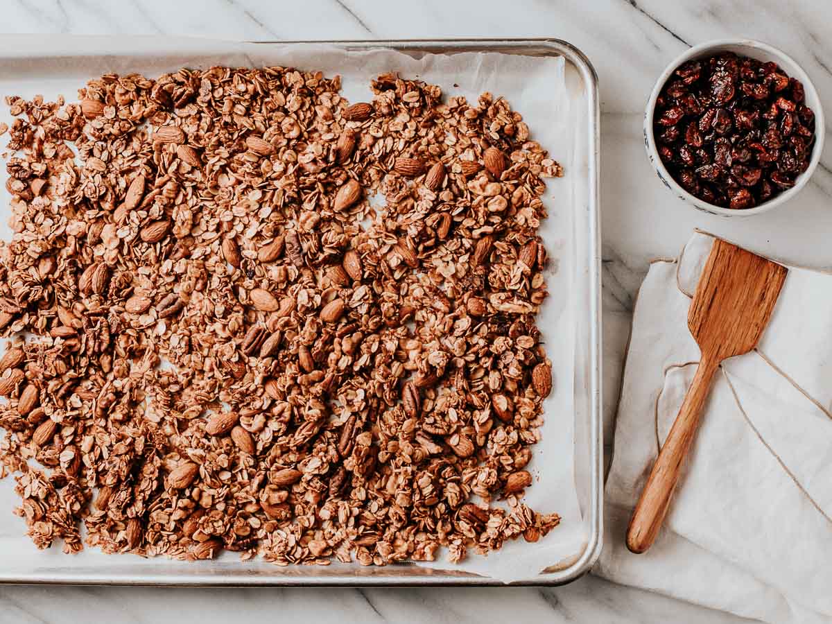 Baked granola on a baking sheet with dried cranberries on the side.