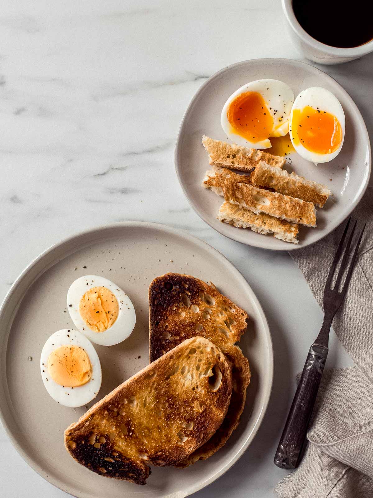 Hard and soft boiled eggs with toast on two plates.