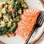 A piece of baked salmon on a plate with broccoli salad.