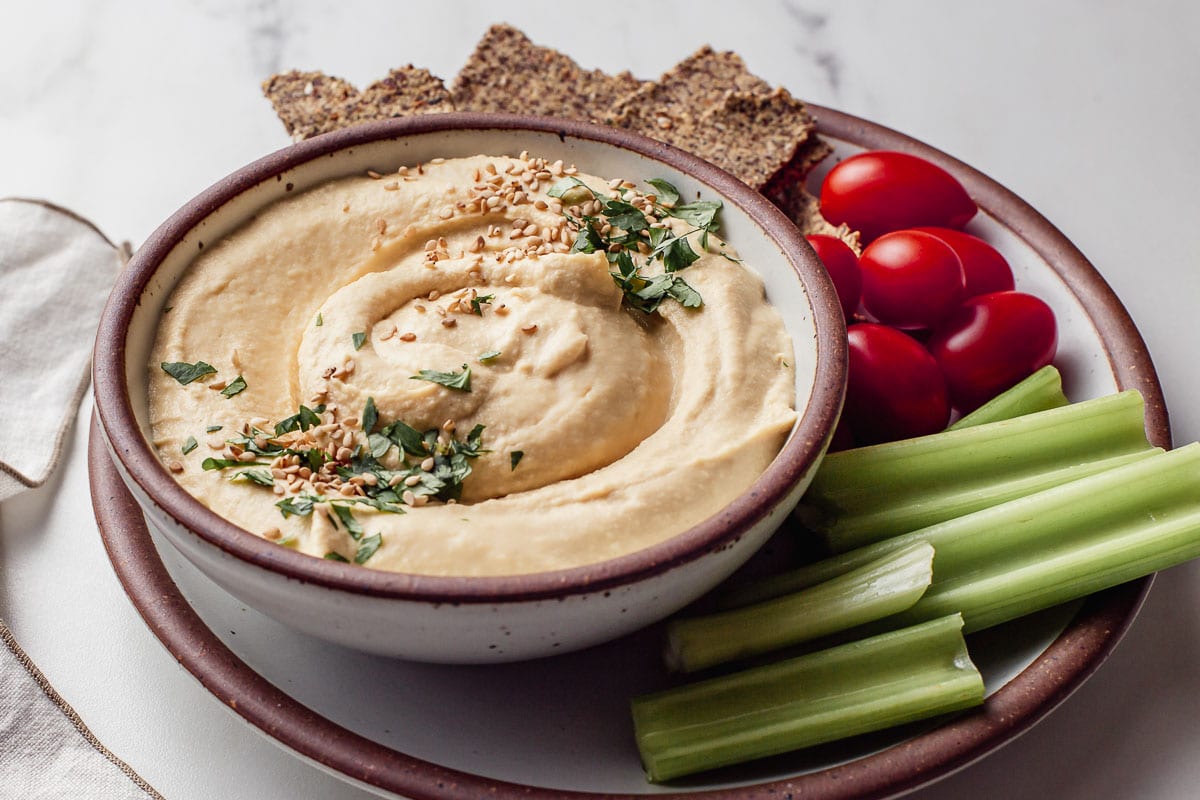 Hummus in a bowl with a side of raw vegetables.